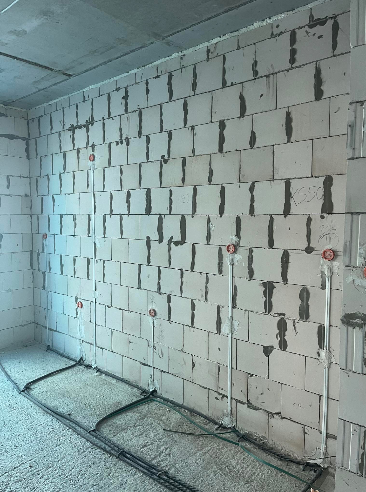 Surowa ściana z betonu komórkowego z widocznymi puszkami i przewodami elektrycznymi w trakcie montażu instalacji w nowym budynku. Detal pionowych bruzd.