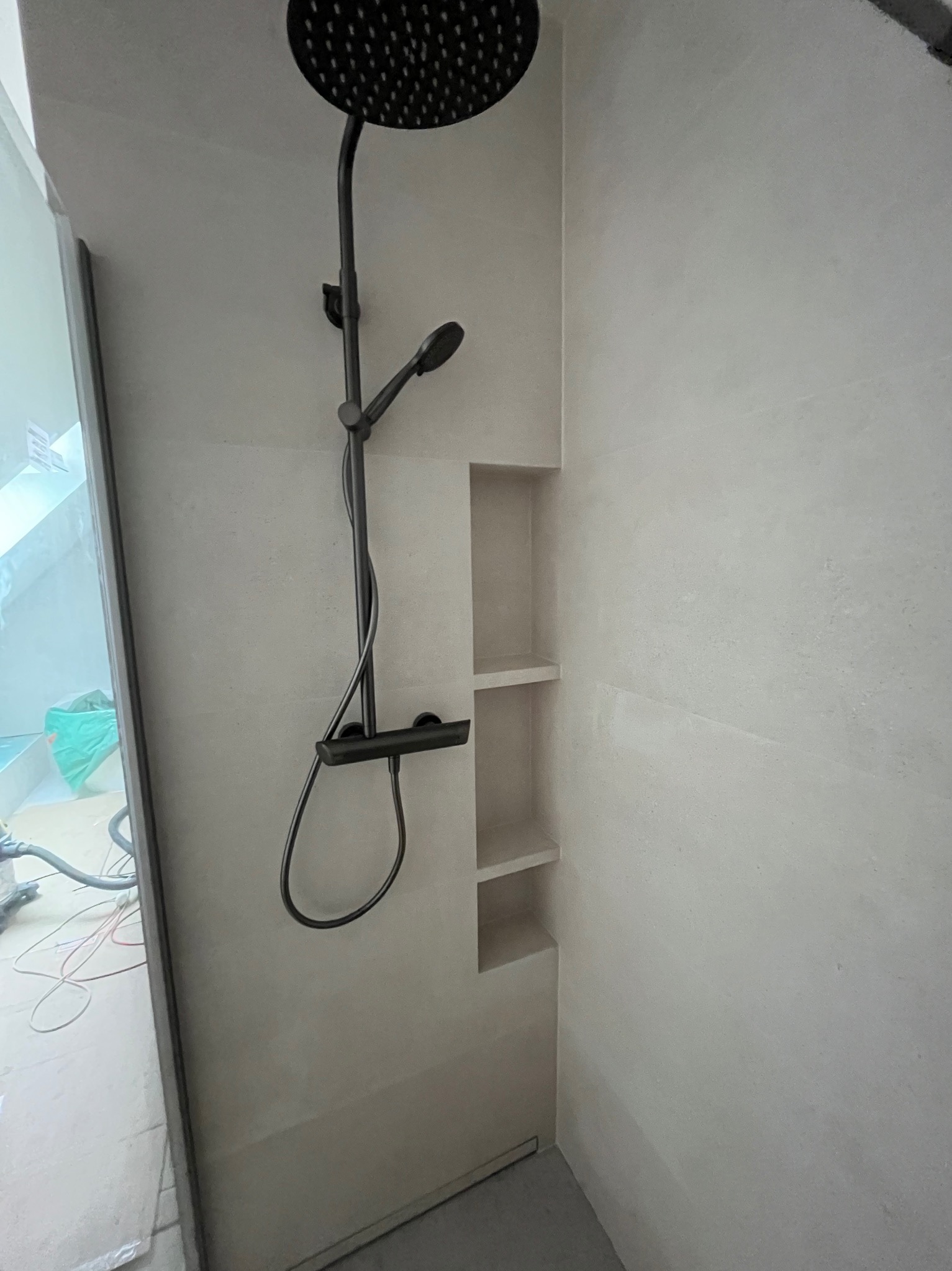 Nowoczesna kabina prysznicowa z deszczownicą w kolorze czarnym i wnękami w ścianie wyłożonej jasnymi płytkami. Minimalistyczny design.