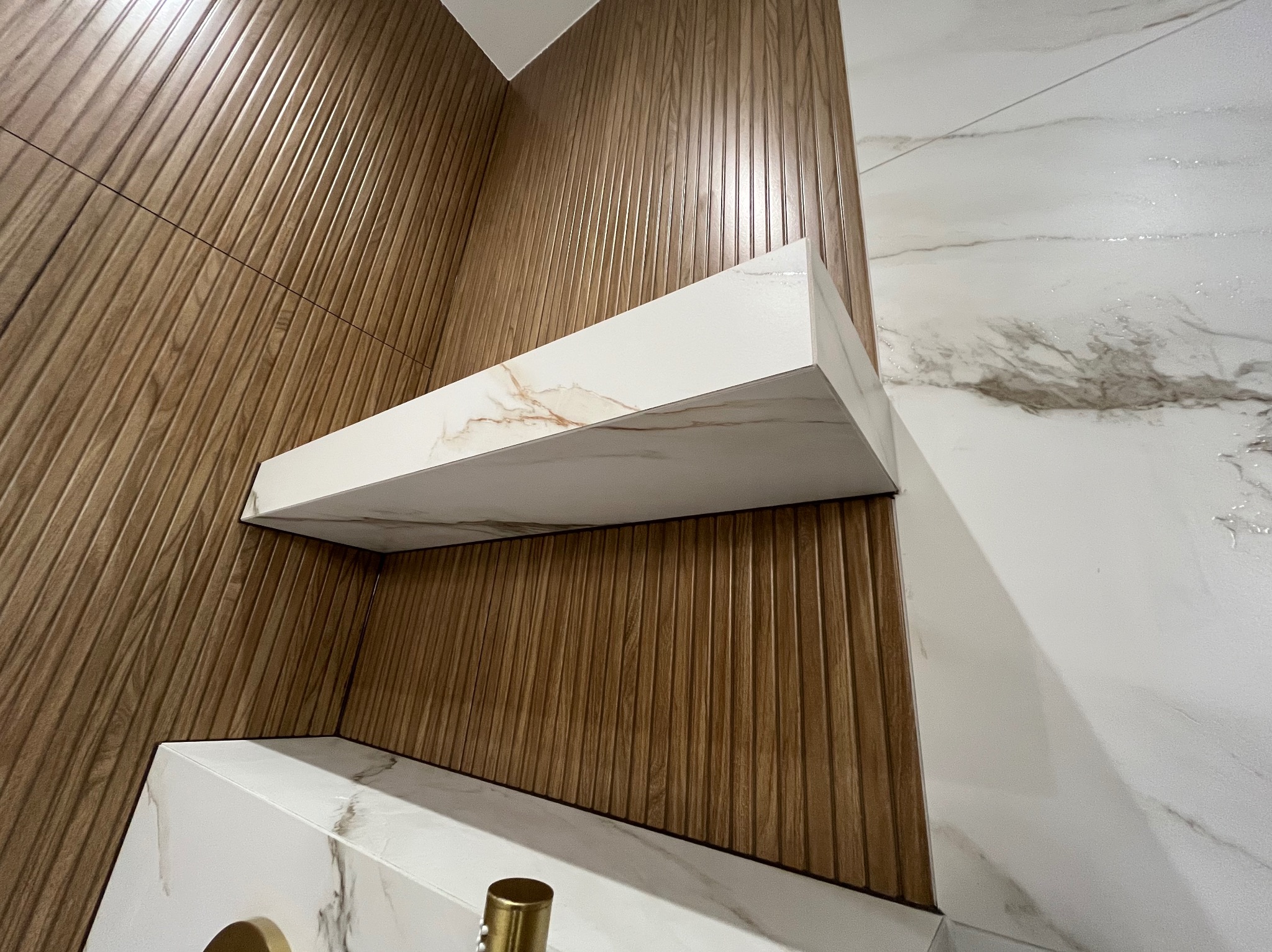 Nowoczesna łazienka z drewnianą ścianą i półkami z marmuru. Minimalistyczny design, eleganckie wykończenie. Ujęcie z dołu podkreśla geometrię wnętrza.
