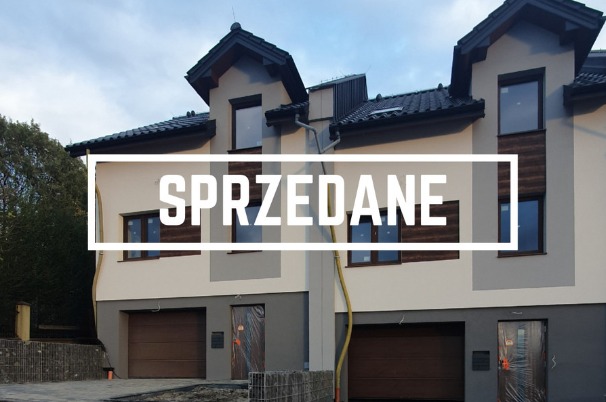 Dwa identyczne, dwukondygnacyjne domy w zabudowie bliźniaczej z garażami, oznaczone napisem 'SPRZEDANE' nałożonym na elewację.