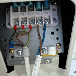 PROinstal - ogrzewanie, chłodnictwo, wentylacja - Podłączenie elektryczne klimatyzatora: widoczne złącza, przewody w różnych kolorach (brązowy, niebieski, zielono-żółty), biała listwa zaciskowa z oznaczeniami.