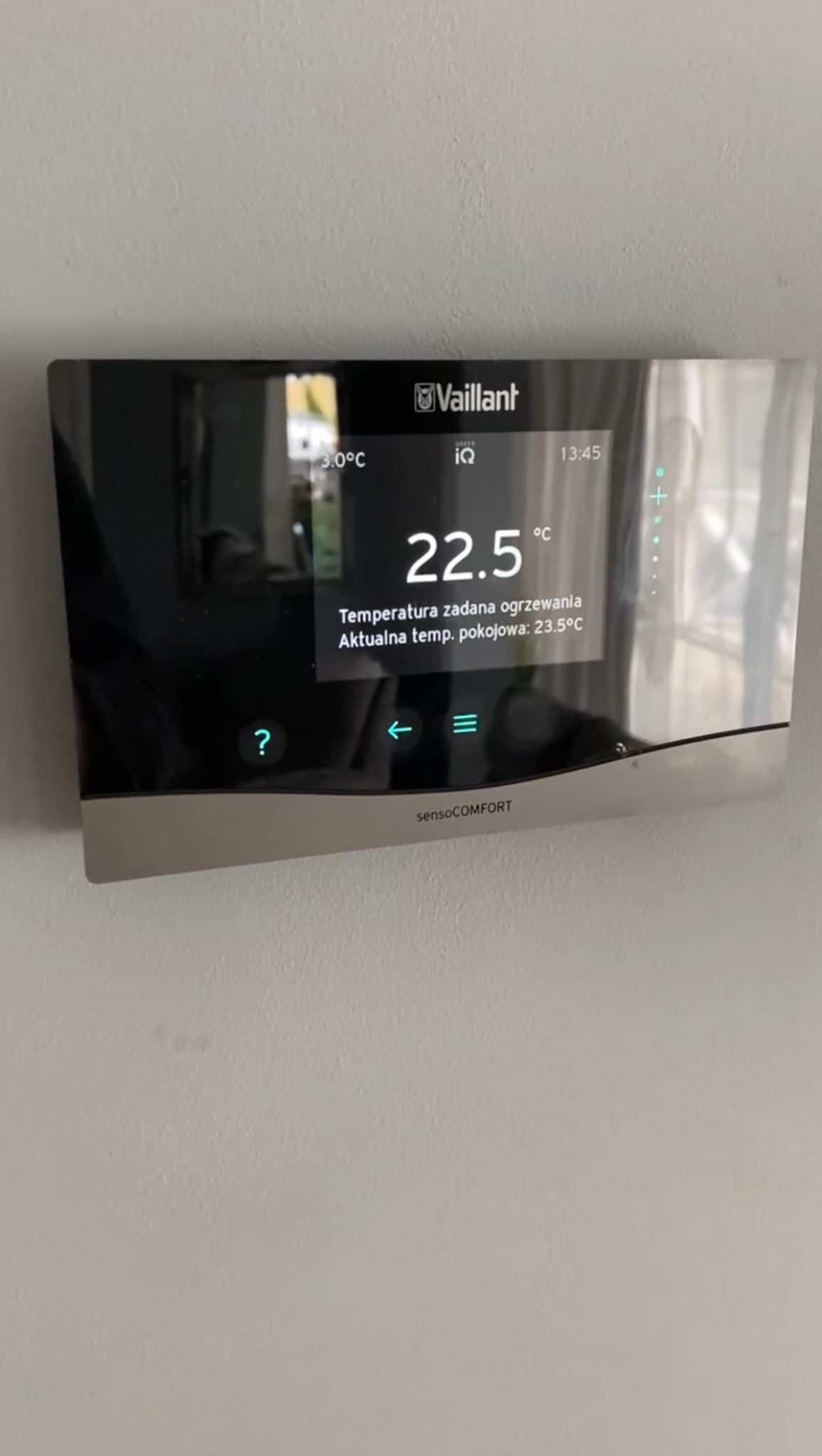 Panel sterowania ogrzewaniem Vaillant sensoCOMFORT z wyświetlaną temperaturą zadaną 22.5°C i aktualną temperaturą pokojową 23.5°C, zamontowany na jasnej ścianie.