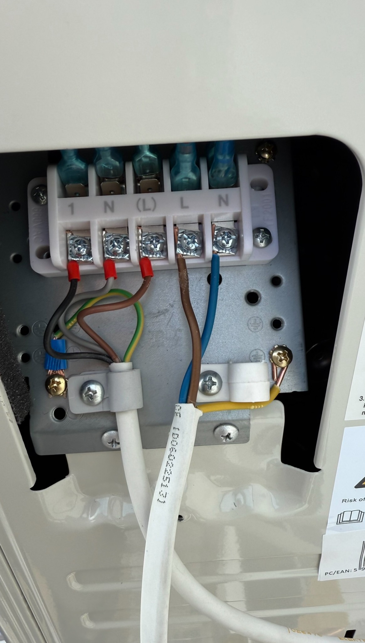 Podłączenie elektryczne klimatyzatora: widoczne złącza, przewody w różnych kolorach (brązowy, niebieski, zielono-żółty), biała listwa zaciskowa z oznaczeniami.