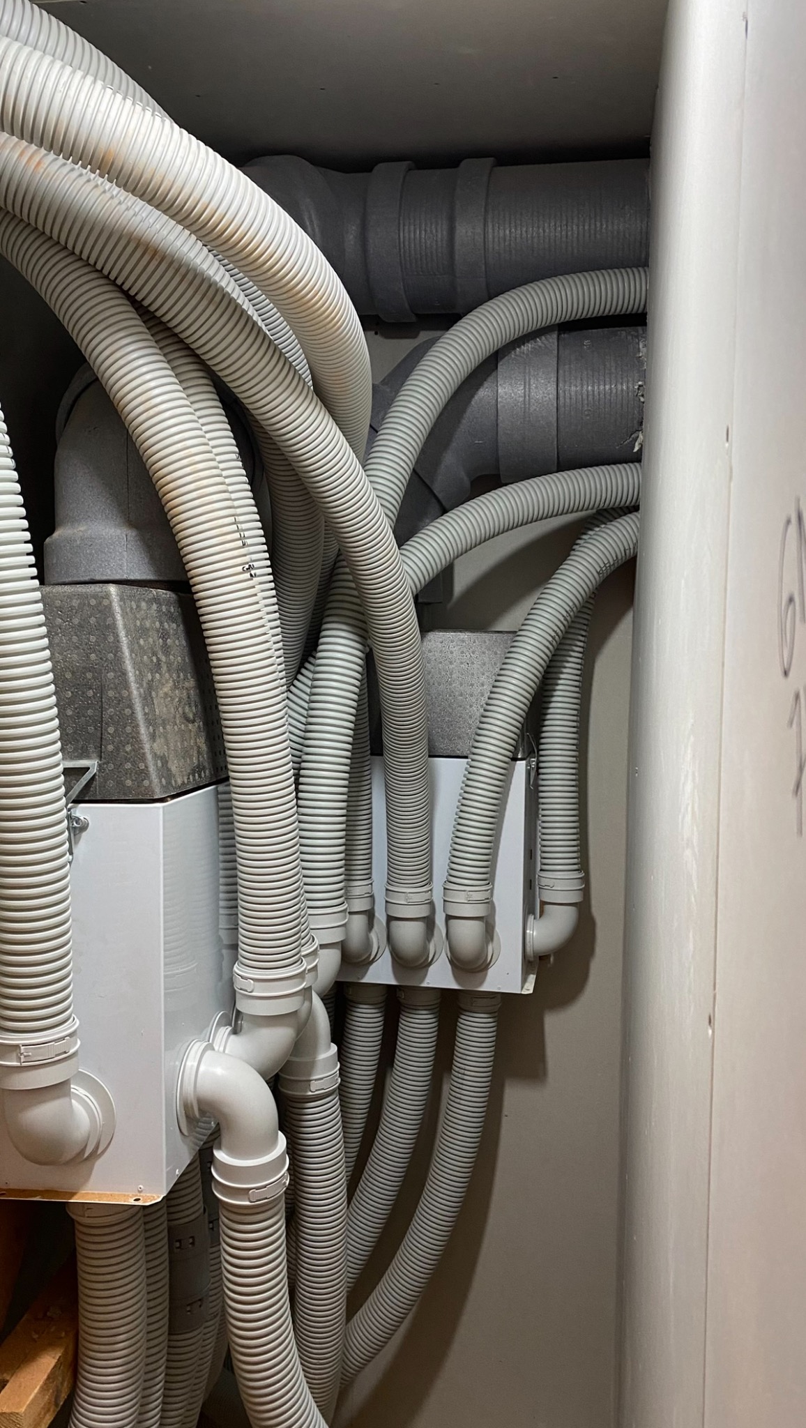 Szczegółowe ujęcie instalacji rekuperacji z licznymi, elastycznymi przewodami wentylacyjnymi w szarym kolorze, prowadzącymi do białych skrzynek rozdzielczych.