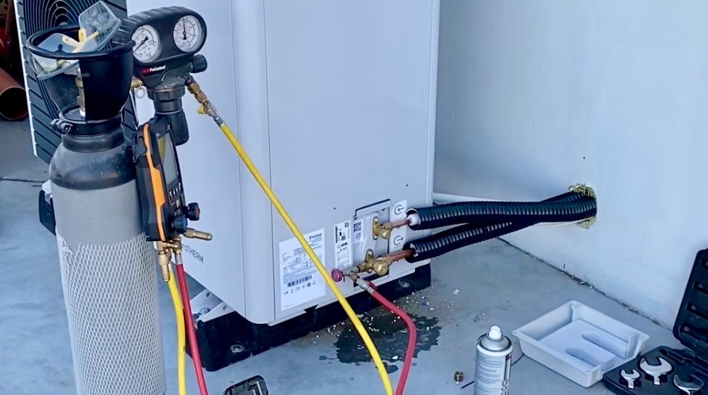 Podłączenie klimatyzacji: butla z gazem, manometry i przewody podłączone do jednostki zewnętrznej klimatyzatora. Widoczne narzędzia i elementy instalacji.