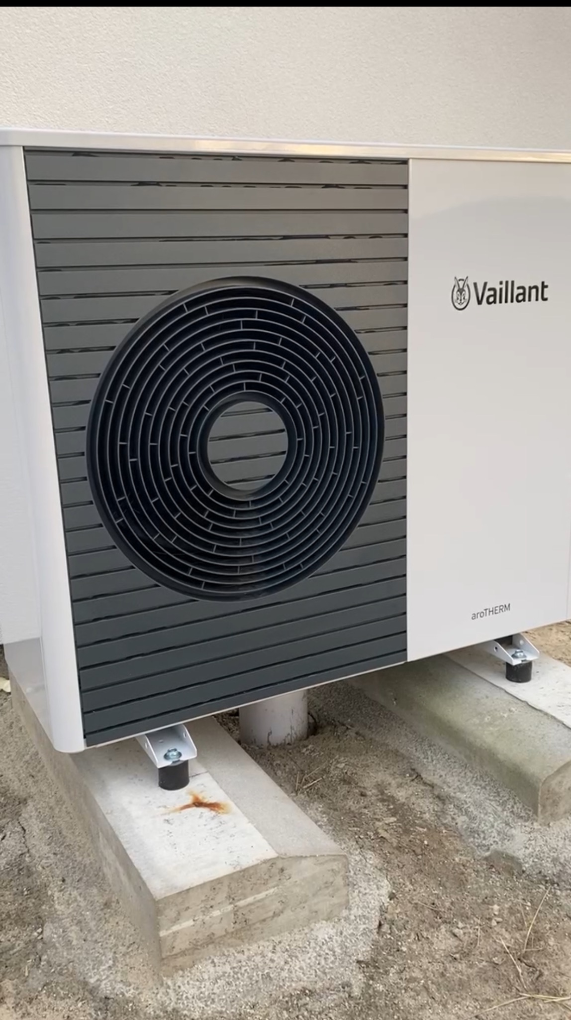 Zamontowana pompa ciepła Vaillant aroTHERM na betonowym fundamencie, widok z boku, z uwzględnieniem detali montażowych i otoczenia.