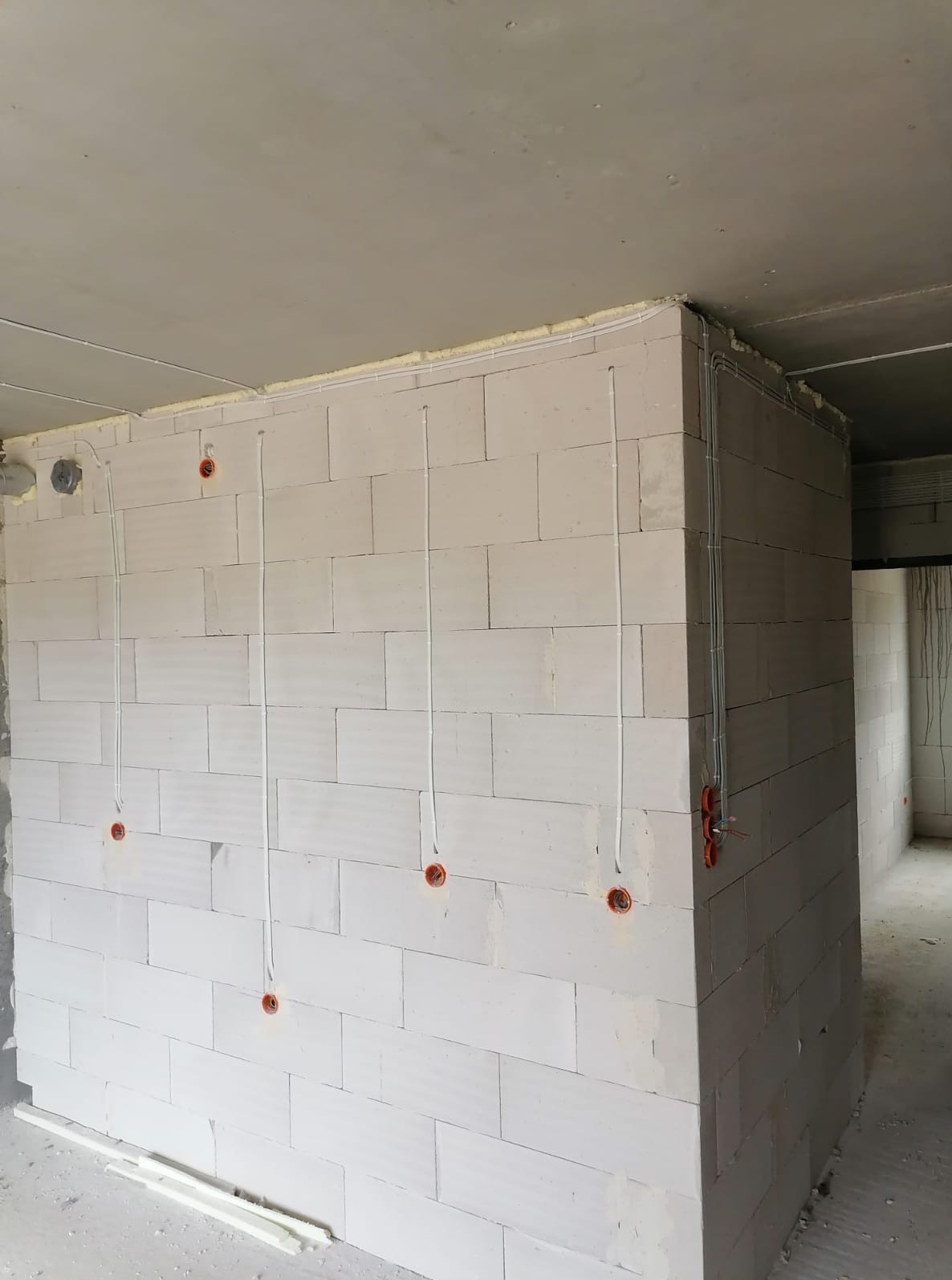 Ściana z betonu komórkowego z pionowo poprowadzonymi przewodami elektrycznymi i puszkami instalacyjnymi, widoczne kable w peszlach przy suficie.