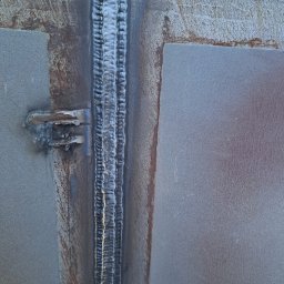 WELT Paweł Brak - Szlifowany spaw na styku dwóch metalowych płyt, widoczne ślady rdzy i niedoskonałości obróbki, surowy industrialny charakter, zbliżenie na spoinę.