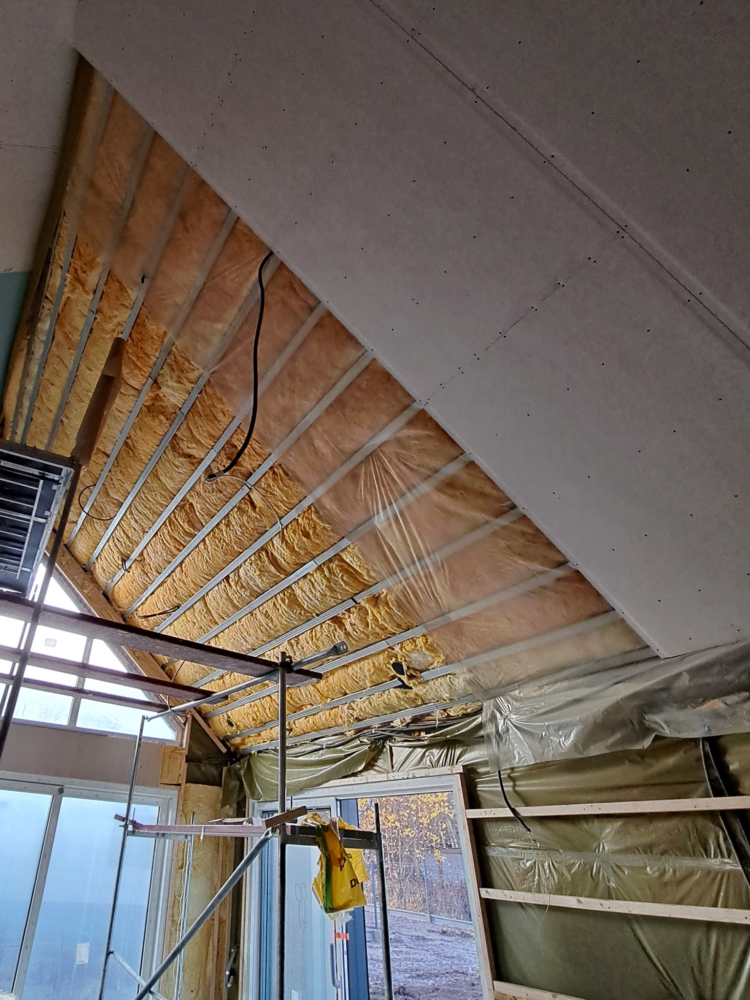 Montaż izolacji i płyt karton-gips na skośnym poddaszu. Widoczne metalowe profile, wełna mineralna i częściowo zamontowane płyty. Prace wykończeniowe w trakcie.