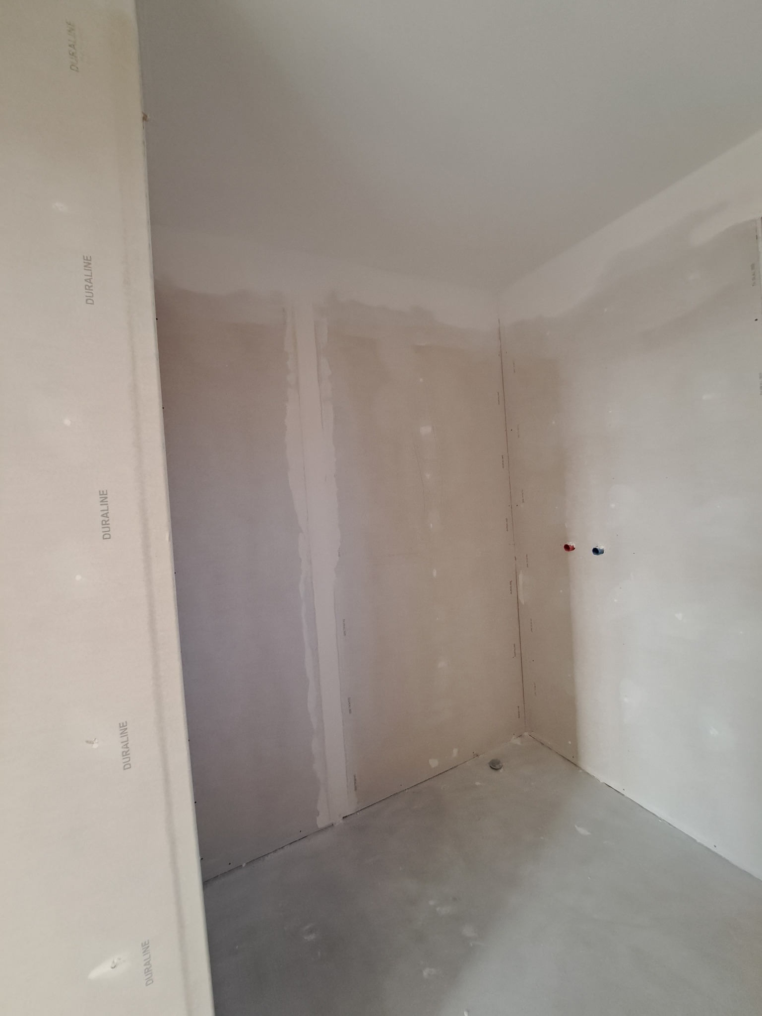 Ściany wykończone płytami gipsowo-kartonowymi, przygotowane do dalszych prac wykończeniowych. Widoczne łączenia płyt i otwory na instalacje. Surowy stan wnętrza.