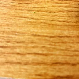 Zbliżenie na drewnianą powierzchnię z wyraźnym rysunkiem słojów. Ciepłe, naturalne odcienie brązu i beżu. Widoczna delikatna, zielona skaza na powierzchni.