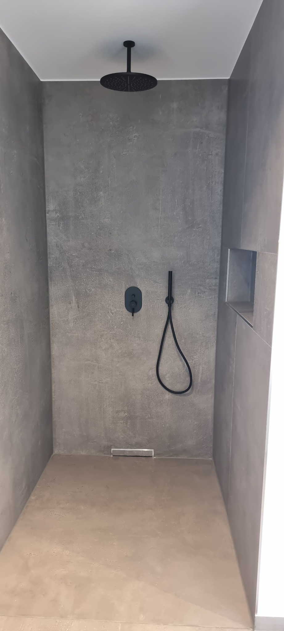 Nowoczesna kabina prysznicowa walk-in z szarą, betonową ścianą i czarną armaturą w Bytomiu. Minimalistyczny design z odpływem liniowym i wnęką na kosmetyki.