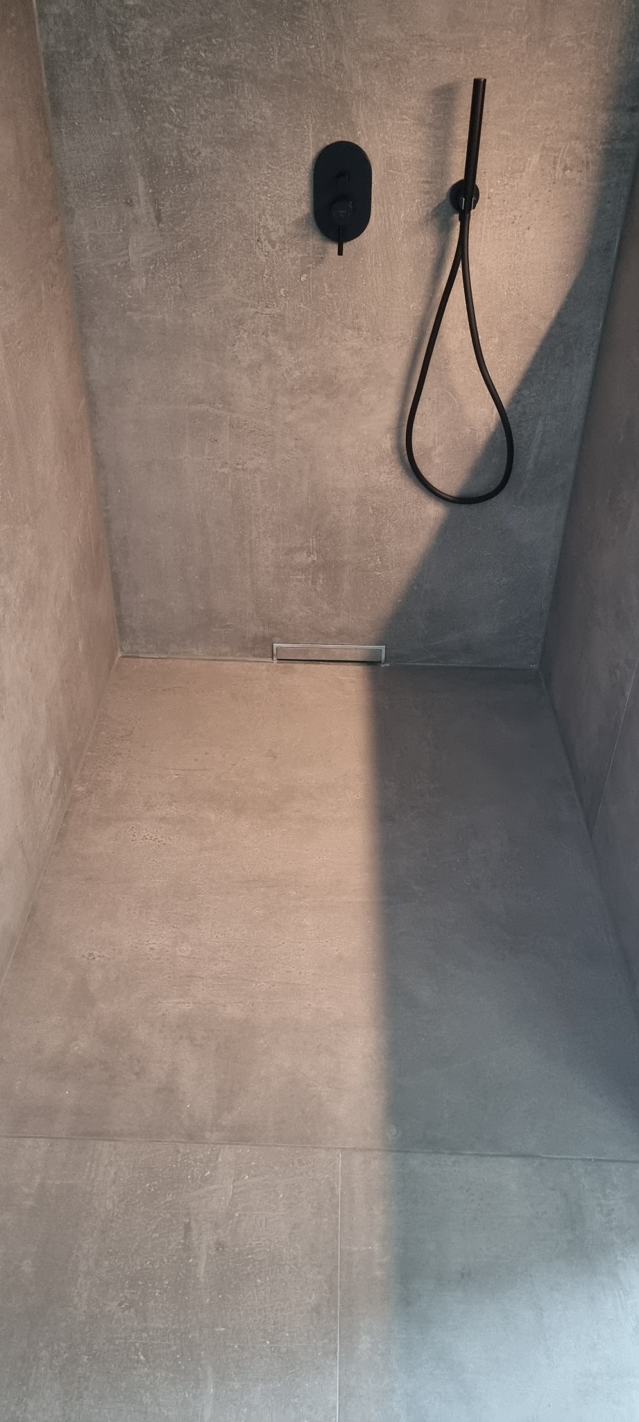 Minimalistyczna kabina prysznicowa z szarymi płytkami, czarną armaturą i odpływem liniowym. Nowoczesny design.