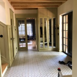 Harmonia Katow - Jasny korytarz z wzorzystą podłogą i drewnianym sufitem. Widoczne drzwi, szafa z lustrami i fragment drabiny malarskiej. Ukończone wykończenie wnętrza.