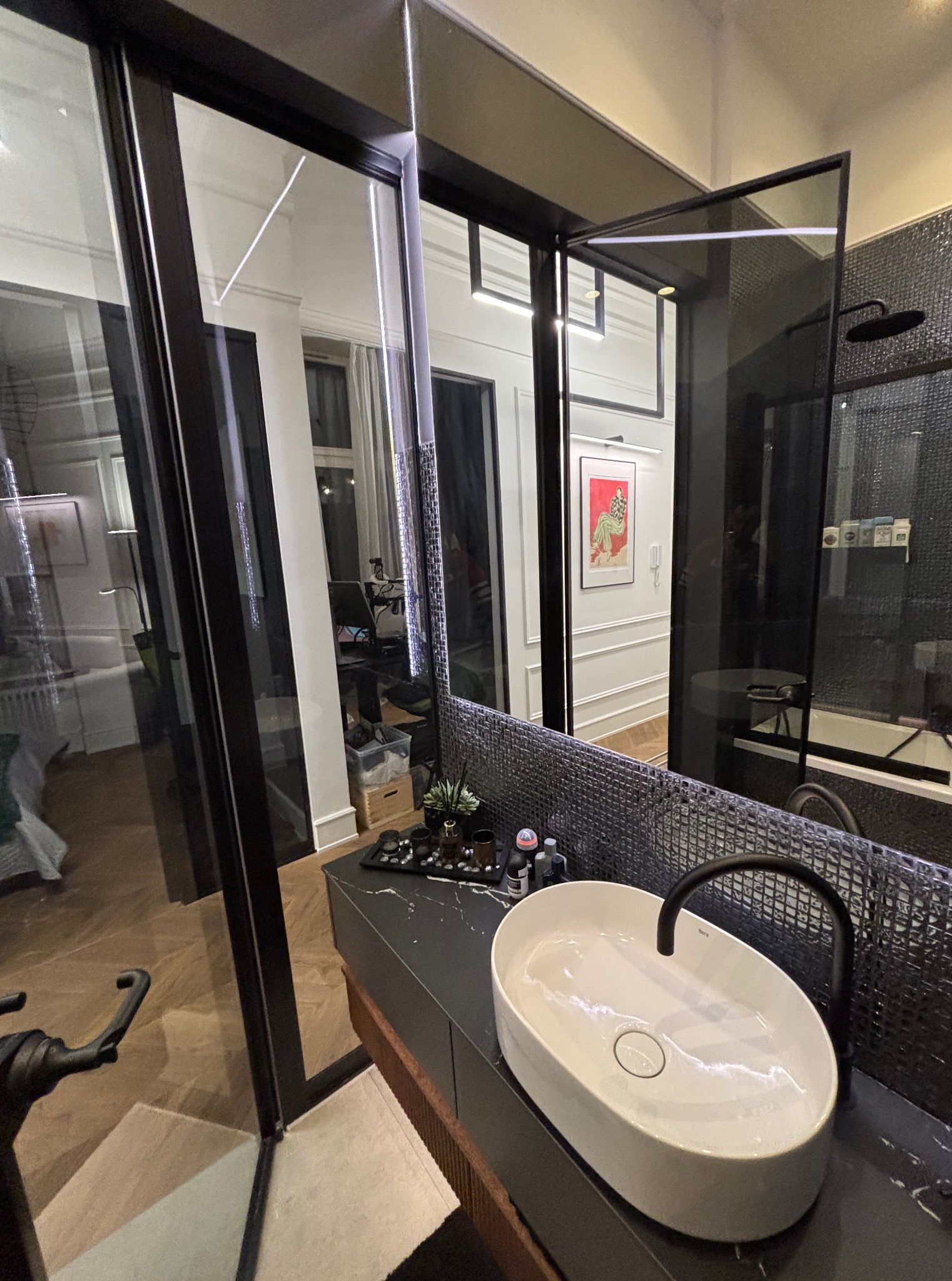 Nowoczesna łazienka z owalną umywalką nablatową, czarną armaturą i mozaikową ścianą. Widok na kabinę prysznicową i przeszklone drzwi.