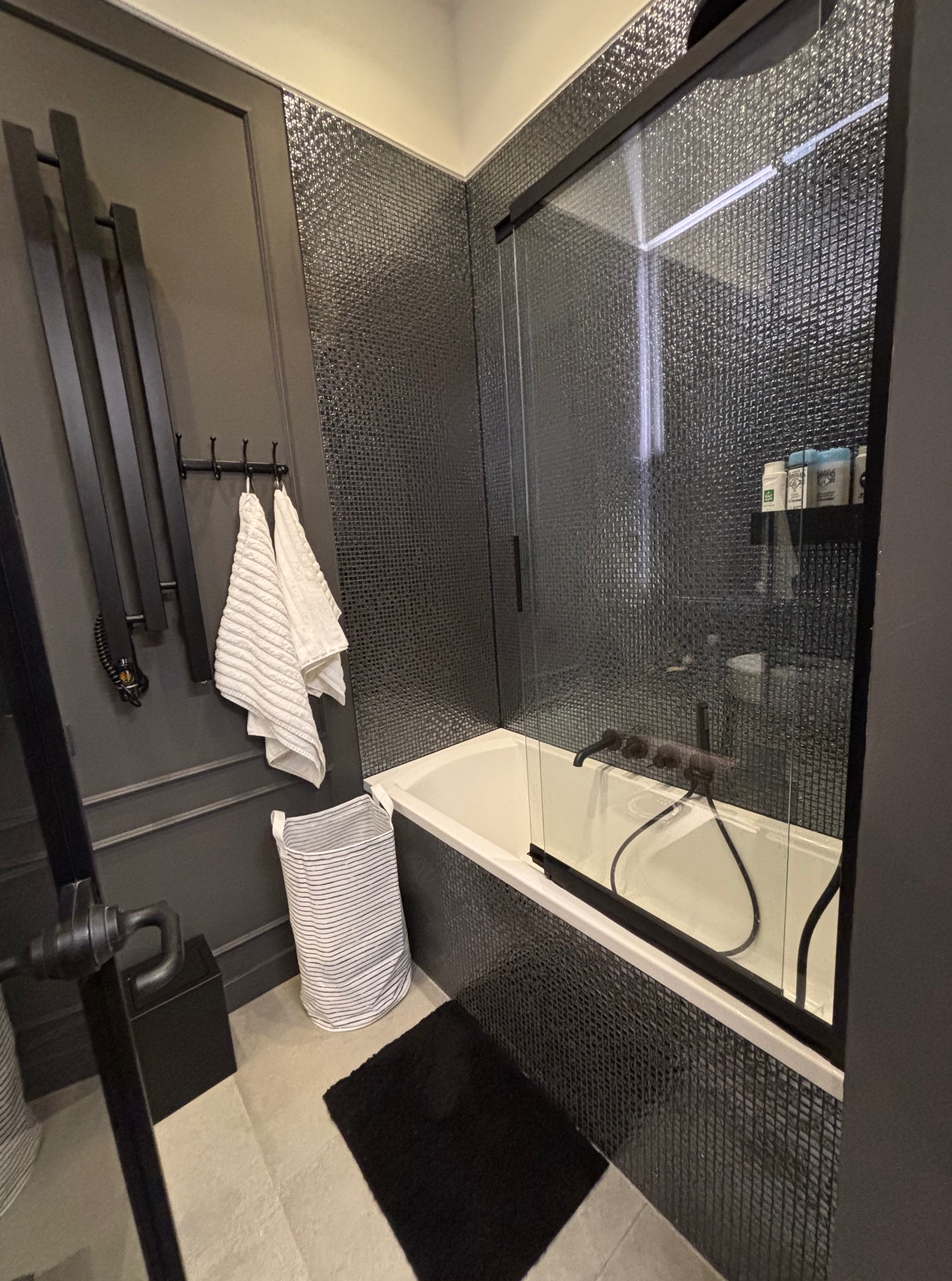 Elegancka łazienka w odcieniach szarości z mozaiką, kabiną prysznicową i grzejnikiem drabinkowym. Minimalistyczny design z akcentami bieli i czerni.