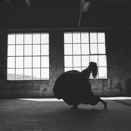 Magdalena Siemaszko Fotografia - Czarno-białe zdjęcie sylwetki kobiety w tańcu na tle okien w opuszczonym budynku. Mocne kontrasty światła i cienia, surowa estetyka wnętrza, ekspresja ruchu i emocji.