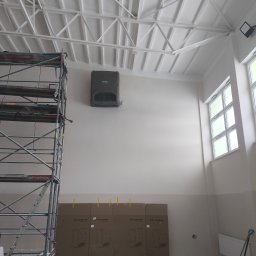 Dar-Max Artsem Churykau - Wnętrze w trakcie montażu wentylacji: widoczne rusztowanie, zamontowany rekuperator na ścianie i kartony z urządzeniami Flowair. Białe ściany i sufit z konstrukcją kratową.