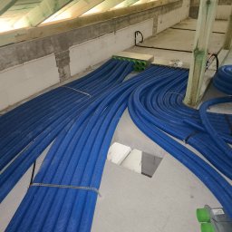 Dar-Max Artsem Churykau - Niebieskie rury wentylacyjne ułożone na poddaszu, widoczne elementy konstrukcji dachu i ściany z betonu komórkowego. Instalacja w trakcie montażu, widok z góry.