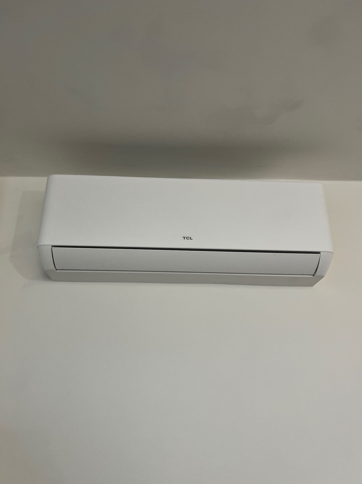 Biały klimatyzator TCL zamontowany na jasnej ścianie w Warszawie. Widok z dołu, centralne ujęcie. Minimalistyczny design, czyste linie.
