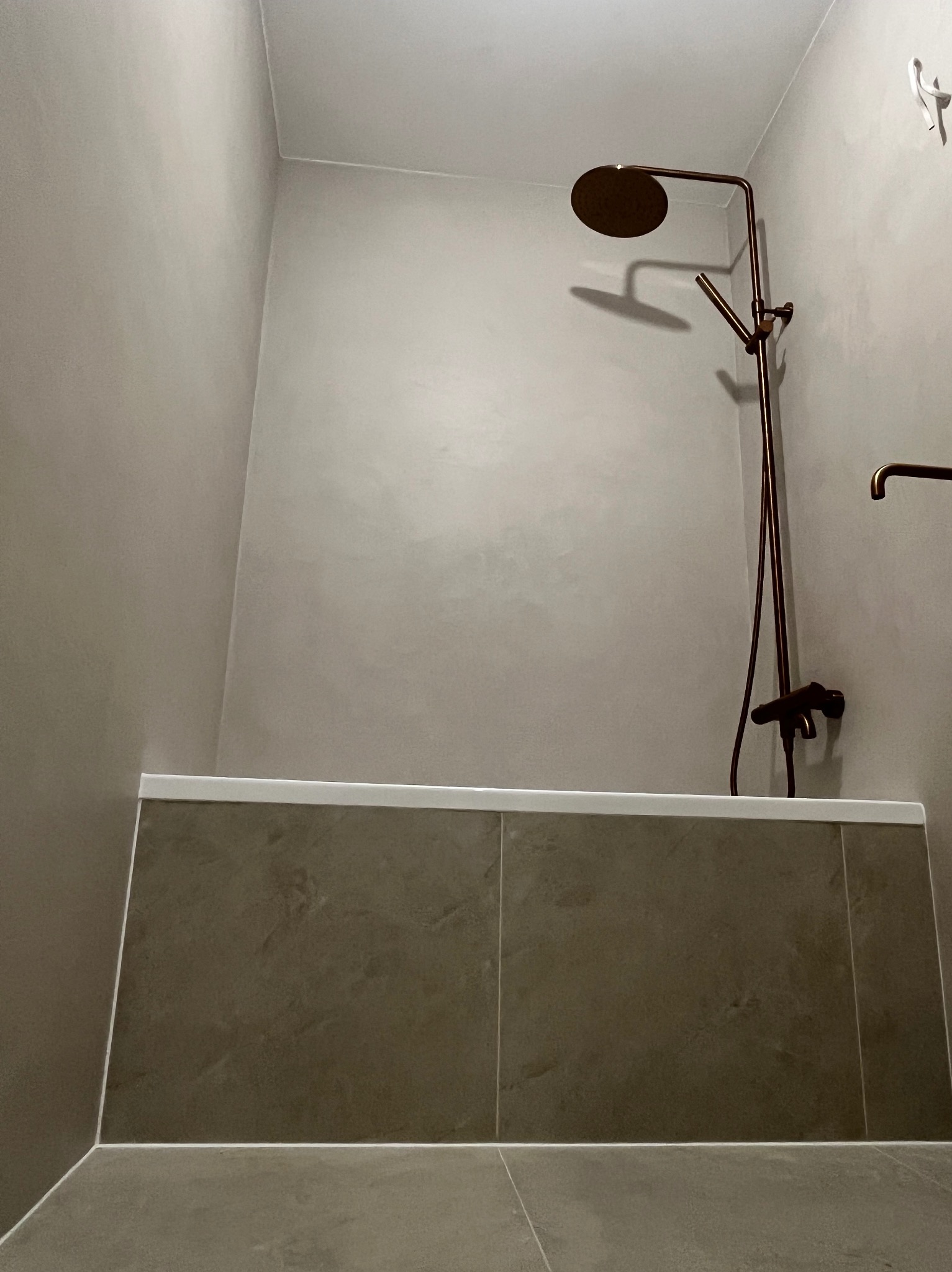 Wykończona łazienka z brązową armaturą i płytkami w odcieniach szarości. Minimalistyczny design, widoczny fragment wieszaka na ręczniki.