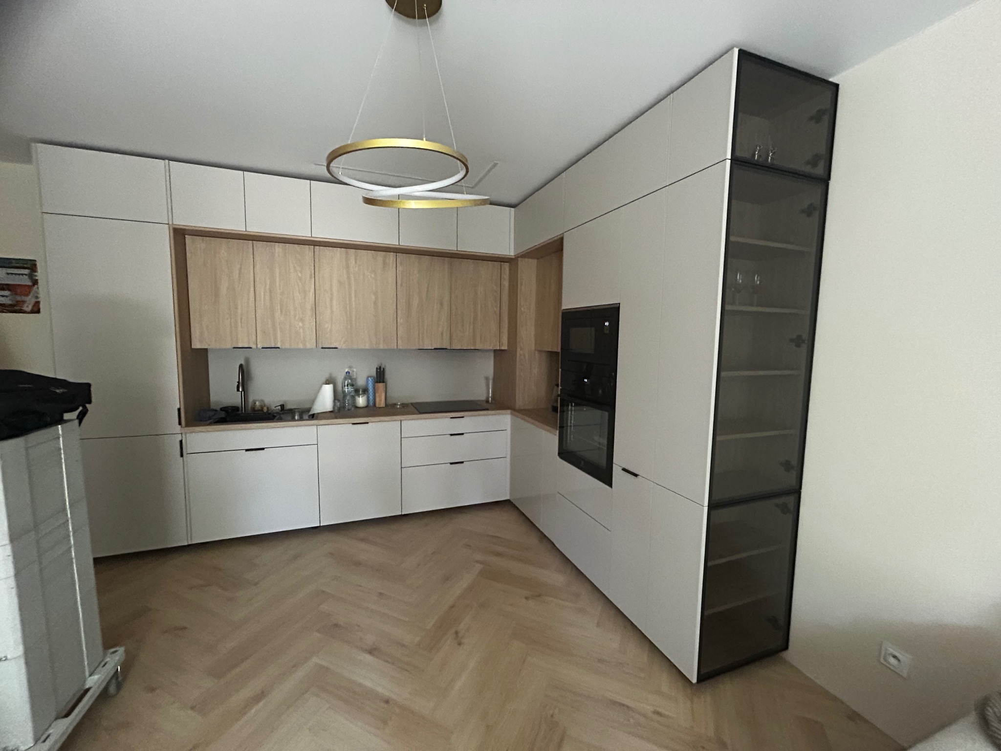 Nowoczesna kuchnia z białymi szafkami dolnymi i drewnianymi górnymi, z oświetleniem LED i szklaną witryną, parkiet w jodełkę na podłodze. Ukończona realizacja.