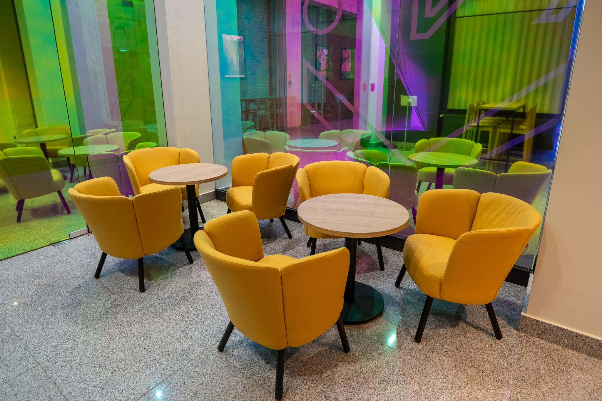 Żółte krzesła i stoliki w przestrzeni eventowej, odbijające się w kolorowej szklanej ścianie. Nowoczesny design i aranżacja wnętrza.
