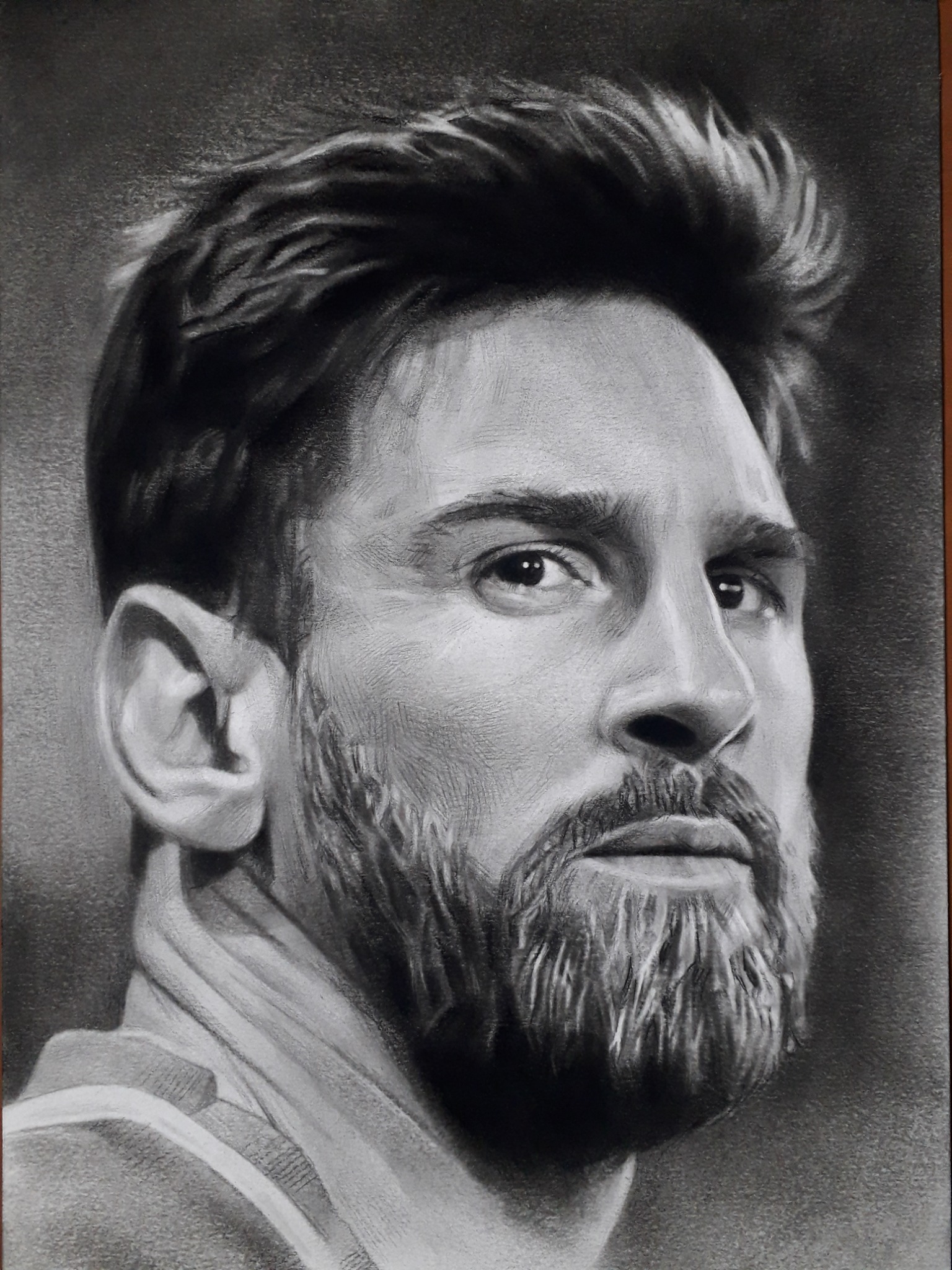 Czarno-biały portret Messiego, wykonany w technice rysunku węglem, z widoczną fakturą papieru i dbałością o detale włosów i zarostu. Profil, zarys ramion.