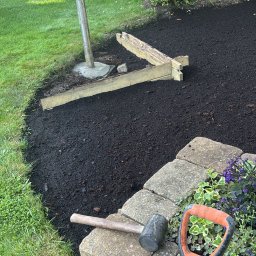 Gaja Gardens Joanna Lalka - Przygotowanie terenu pod rabatę: świeżo rozsypana kora, obrzeże z kostki, narzędzia ogrodnicze (szpadel, młotek) i lampa ogrodowa w tle.