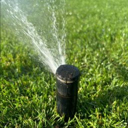 Gaja Gardens Joanna Lalka - Automatyczny zraszacz trawnikowy w akcji, rozpylający wodę na soczystą, zieloną trawę. System nawadniania w ogrodzie.