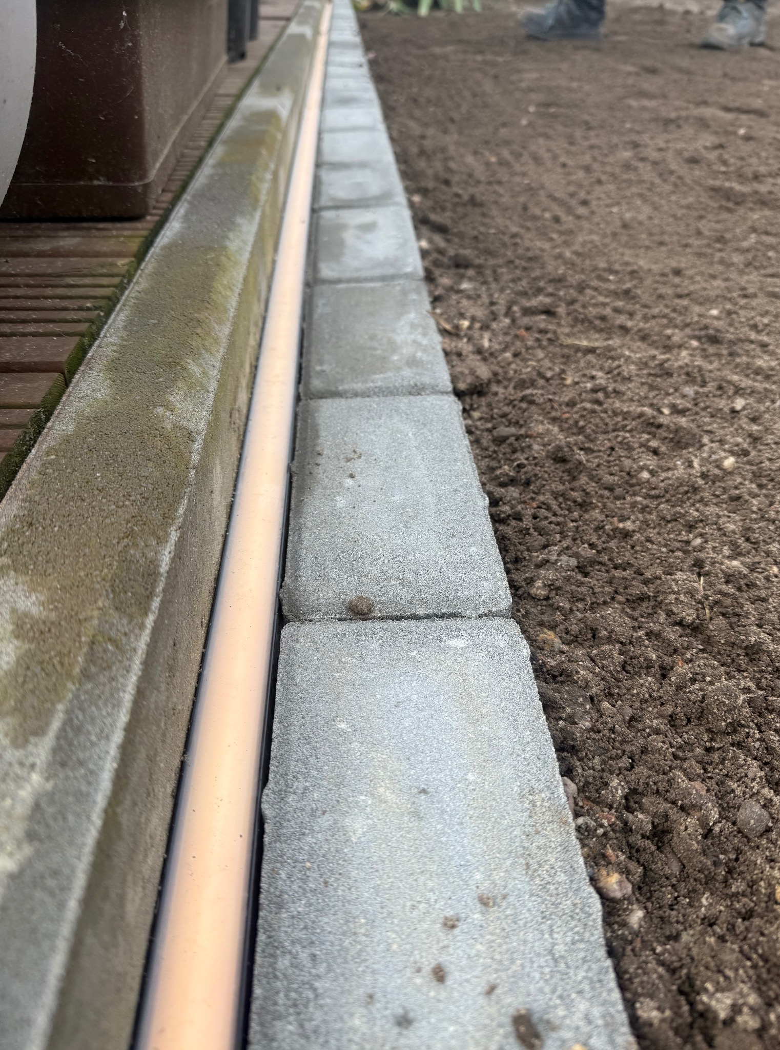 Krawężnik z kostki brukowej oddzielający rabatę od tarasu. Widoczna rura drenażowa. Przygotowanie podłoża pod nasadzenia.