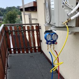 VG sp. z o.o. - Serwis klimatyzacji Kaisai na balkonie: podłączone manometry, widoczne przewody w kolorach żółtym, niebieskim i czerwonym. Zewnętrzna jednostka klimatyzatora na ścianie.