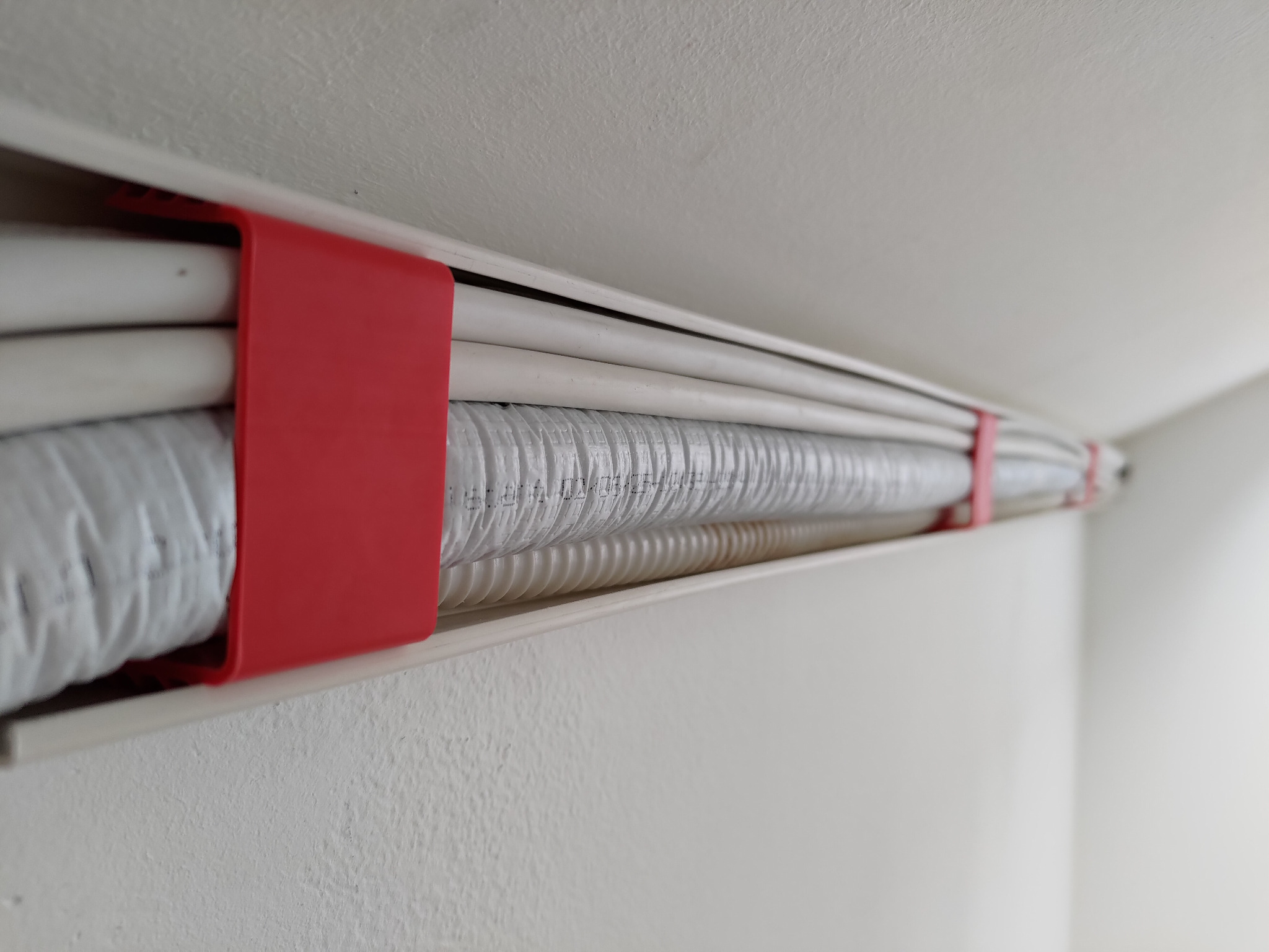 Białe przewody w korytku przymocowanym do sufitu, zabezpieczone czerwonymi uchwytami. Instalacja elektryczna w nowym budynku.