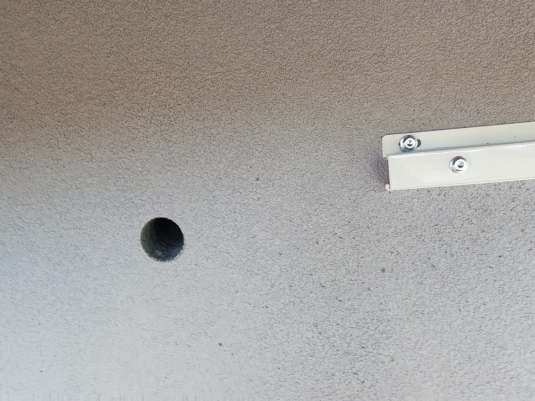 Otwór w ścianie obok zamocowanego wspornika klimatyzacji. Przygotowanie do montażu klimatyzatora, widoczna struktura ściany zewnętrznej.