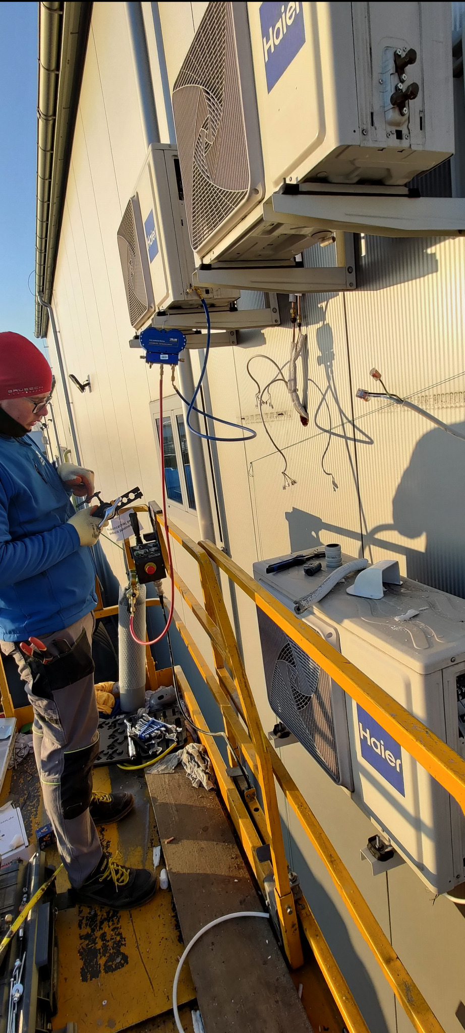 Monteraż klimatyzacji Haier na zewnątrz budynku. Widoczne narzędzia, przewody i elementy instalacji. Praca na wysokości, zabezpieczona barierkami.