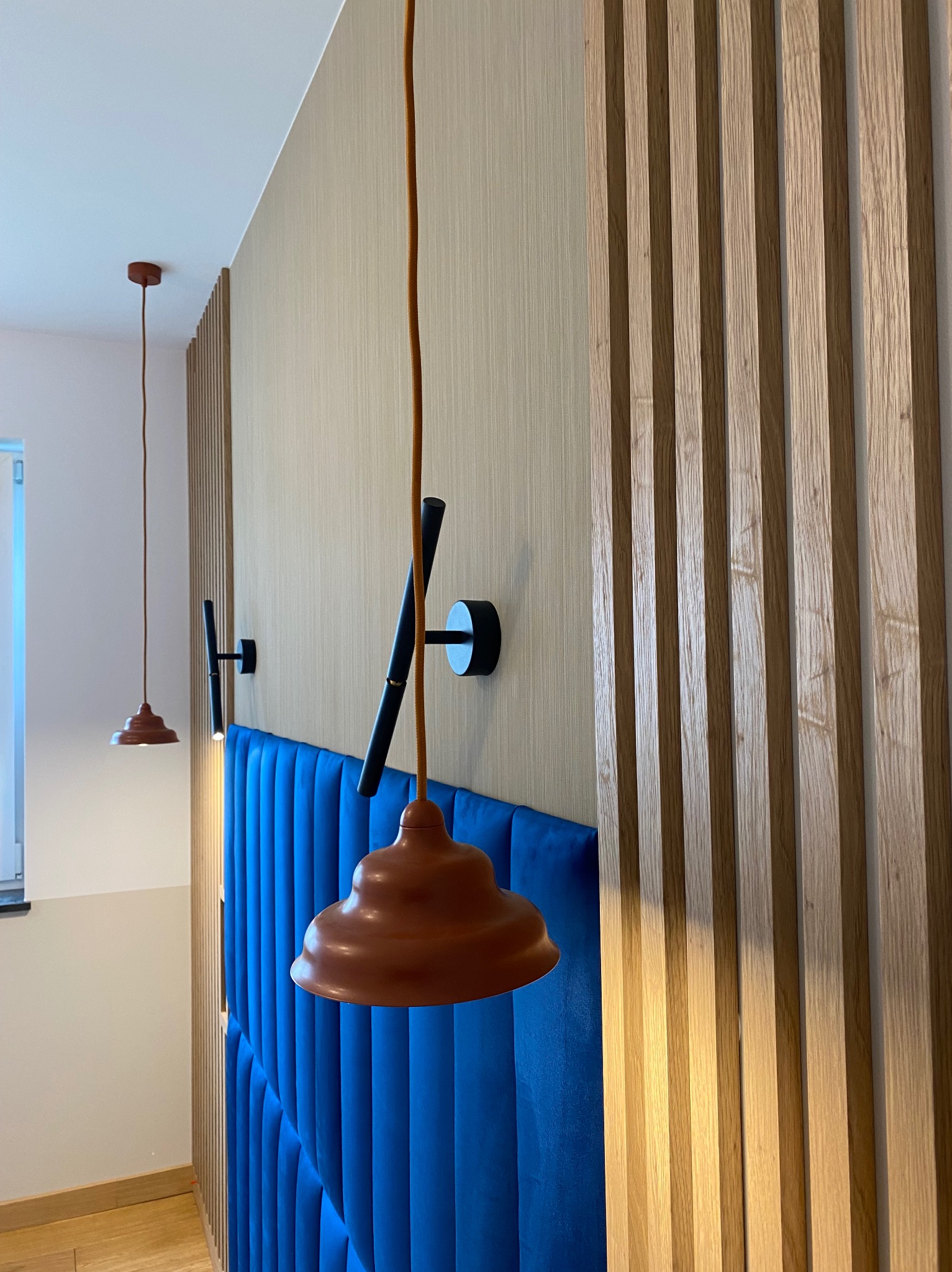 Niebieski tapicerowany zagłówek z oświetleniem punktowym i drewnianą ścianką działową. Nowoczesny design sypialni z detalami wykończeniowymi.