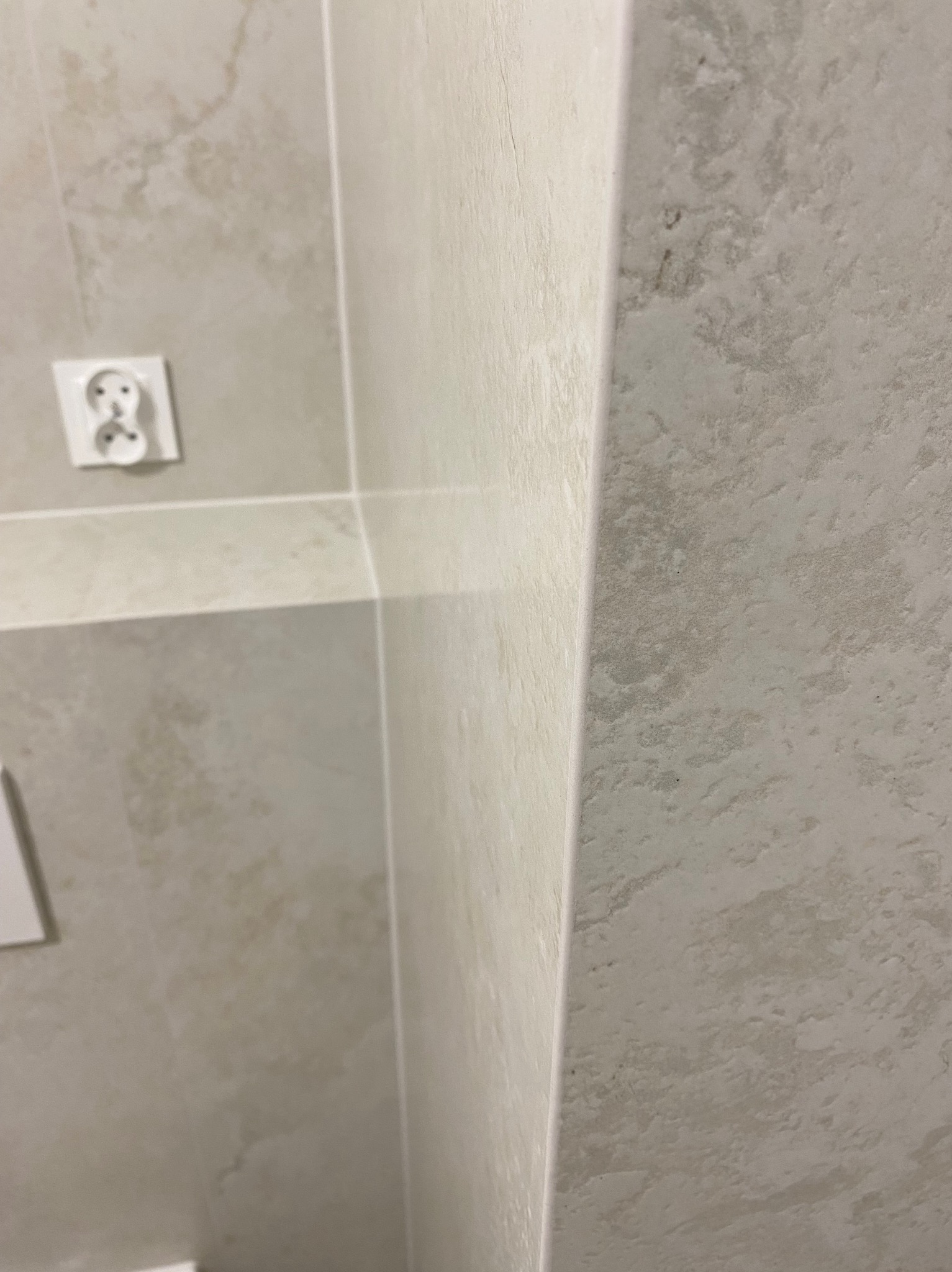Beżowa, marmurkowa ściana łazienki z gniazdkiem elektrycznym. Widoczny styk dwóch ścian pod kątem prostym, fuga. Minimalistyczny design wnętrza.