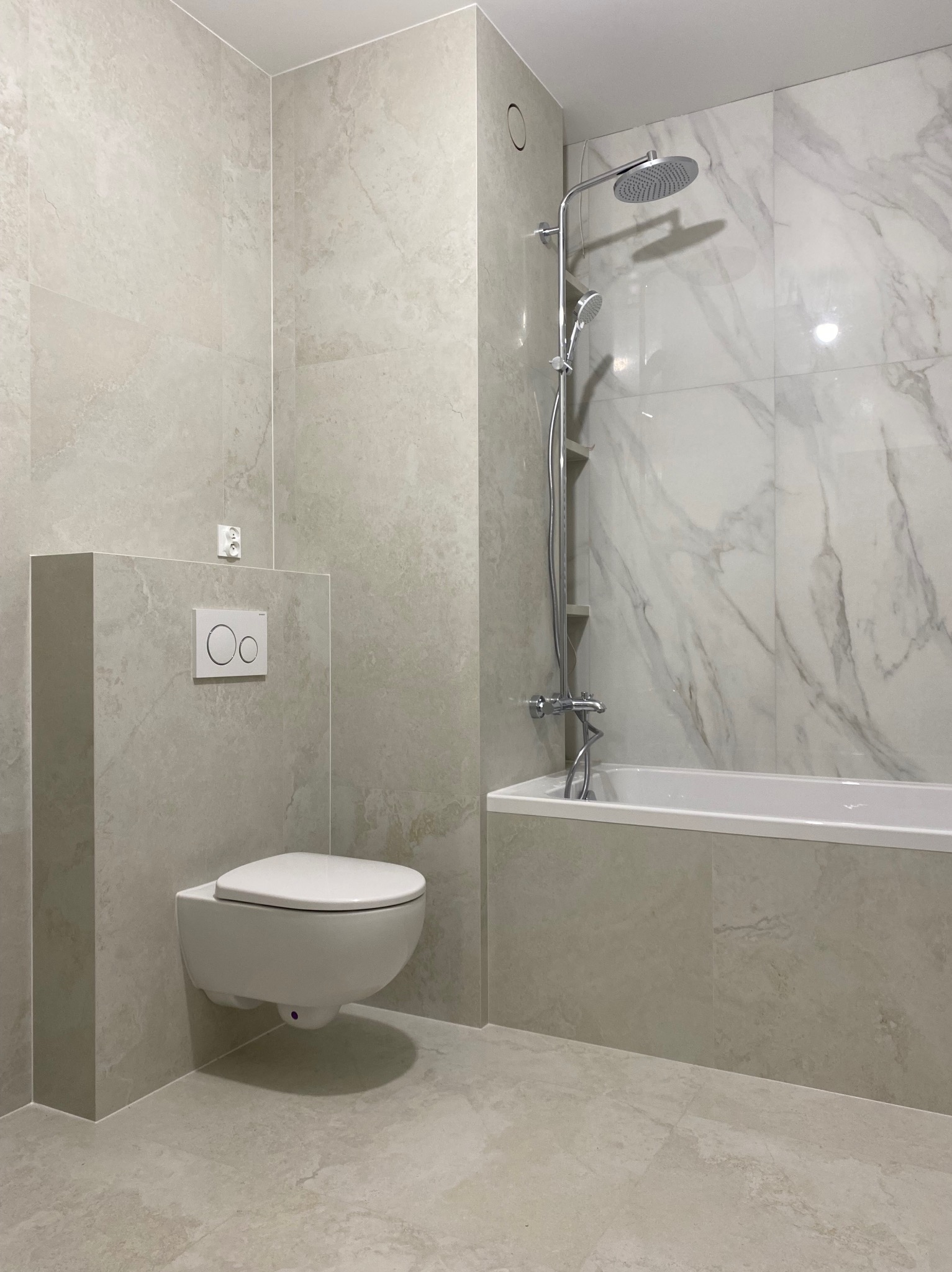 Jasna łazienka po remoncie: beżowe płytki imitujące marmur na ścianach i podłodze, podwieszana toaleta, bateria prysznicowa i wanna. Minimalistyczny design.