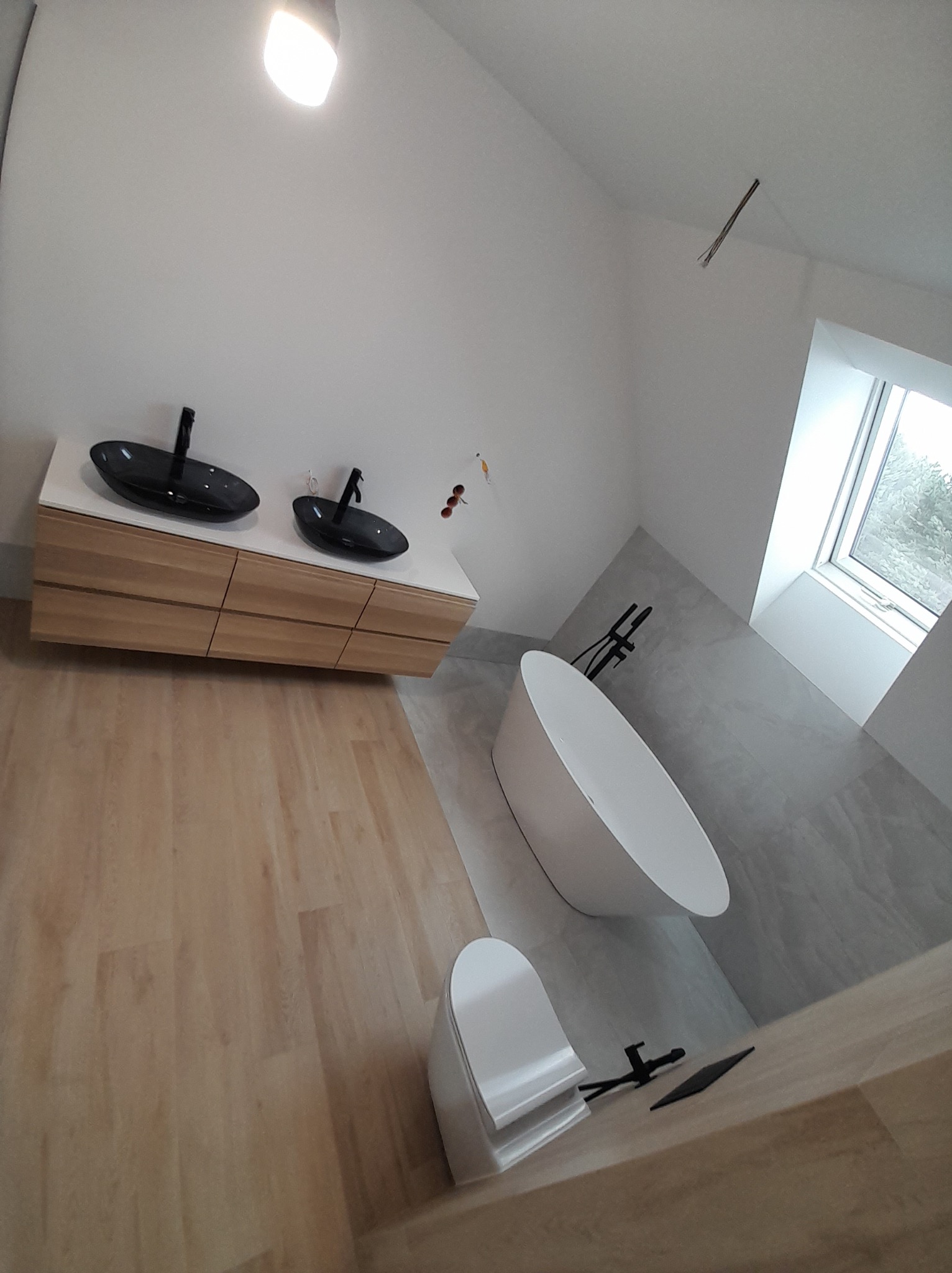 Nowoczesna łazienka z wolnostojącą wanną, umywalkami nablatowymi i drewnianą podłogą. Minimalistyczny design z oknem wpuszczającym naturalne światło.