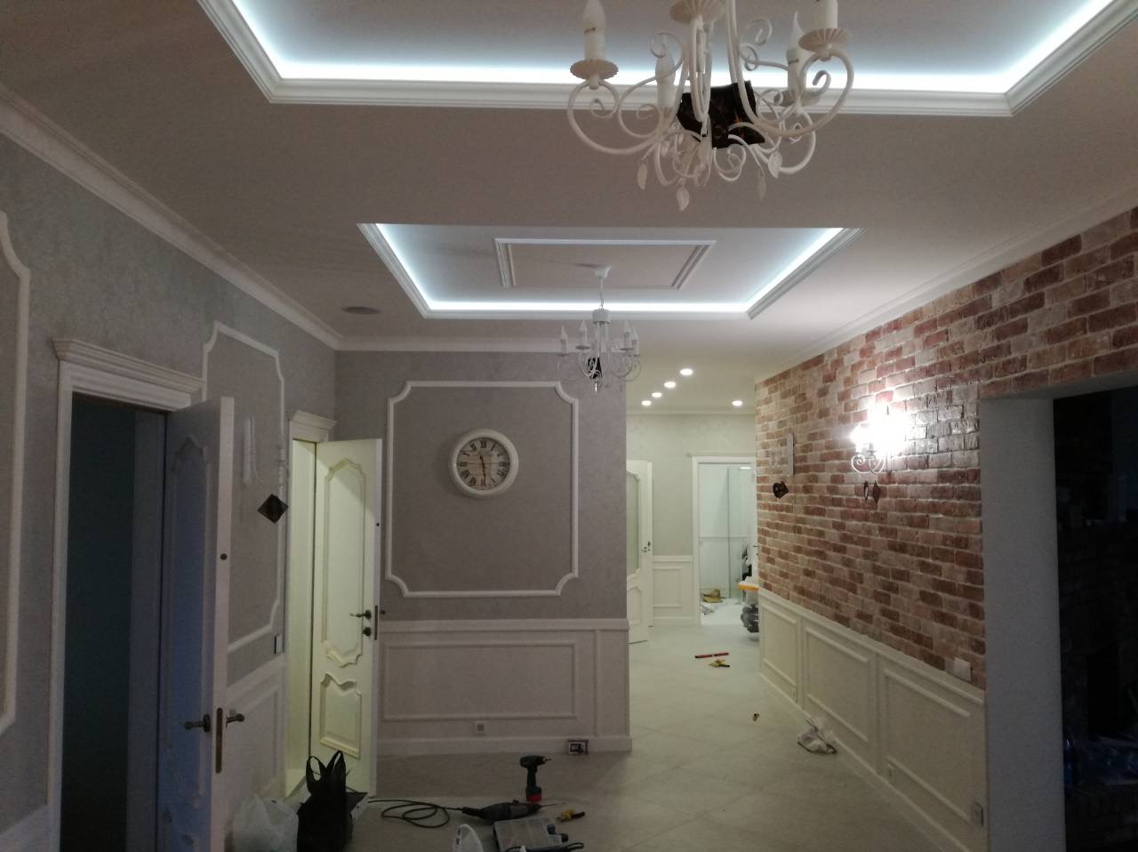 Eleganckie wykończenie wnętrza w Gdańsku: dekoracyjne sztukaterie, oświetlenie sufitowe LED i ściana z cegły, tworzące unikalny efekt wizualny.