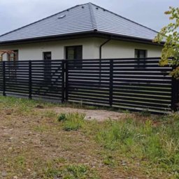 STREFA OGRODZEŃ - Nowoczesne, poziome ogrodzenie metalowe w kolorze czarnym, z widocznym domem w tle. Minimalistyczny design i staranne wykonanie.