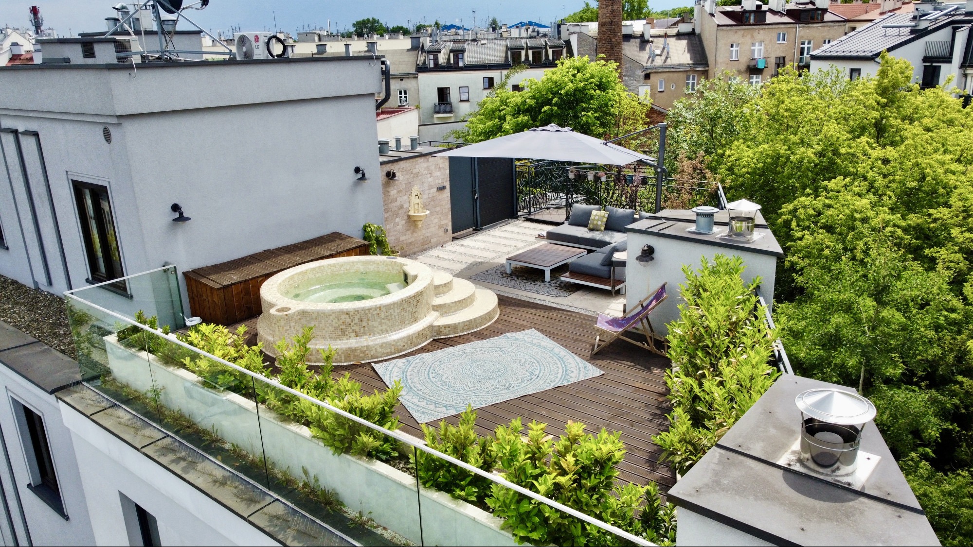 Luksusowy taras na dachu z jacuzzi, meblami wypoczynkowymi i zielenią. Widok z góry na nowoczesną aranżację przestrzeni relaksu w miejskiej scenerii.