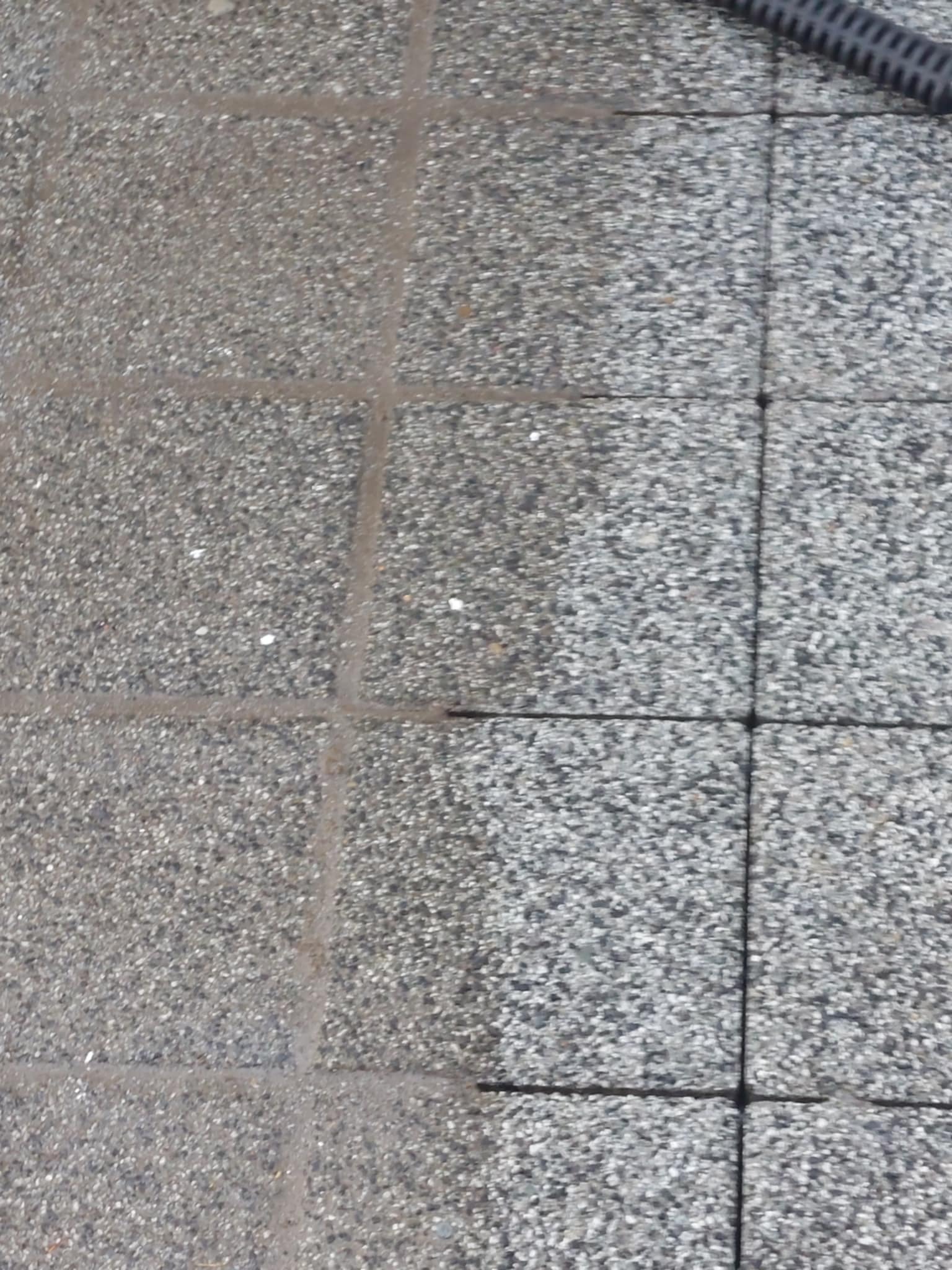 Fragment kostki brukowej, z widoczną różnicą w czystości po prawej stronie; czyszczenie pod ciśnieniem, dysza węża w prawym górnym rogu kadru.