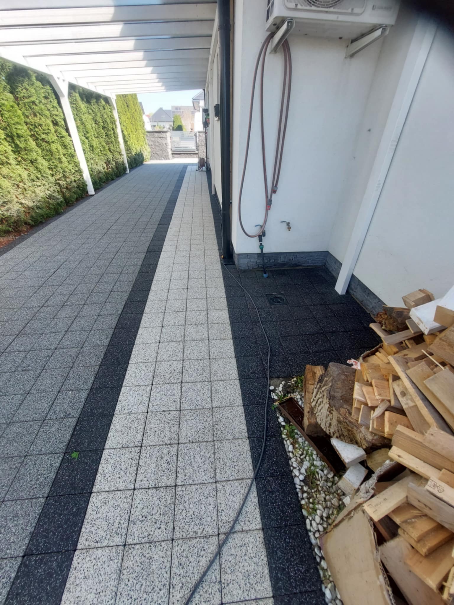 Dwukolorowa kostka brukowa na podjeździe z widocznym zanieczyszczeniem i resztkami drewna, sugerującymi potrzebę czyszczenia.