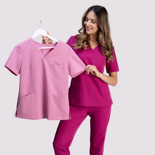 Modelka prezentuje komplet odzieży medycznej w kolorze fuksji. Obok, na wieszaku, bluzka medyczna w odcieniu pudrowego różu. Stonowane tło, profesjonalna prezentacja.