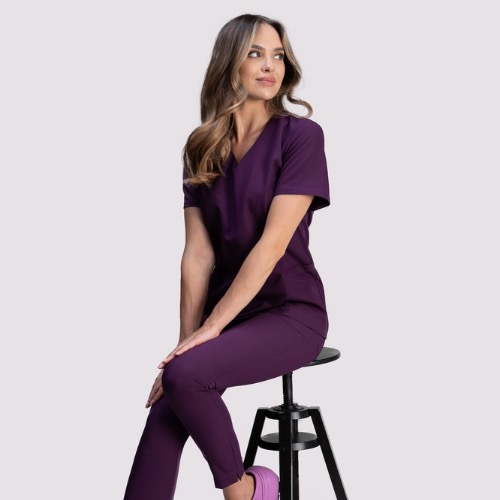 Kobieta siedzi na stołku, prezentując śliwkowy komplet odzieży roboczej z krótkim rękawem i spodniami. Uzupełnieniem są fioletowe buty.