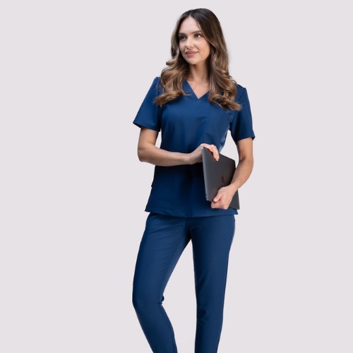 Uśmiechnięta kobieta w granatowym komplecie medycznym, trzymająca laptopa, prezentuje profesjonalny wygląd w gabinecie lub klinice.