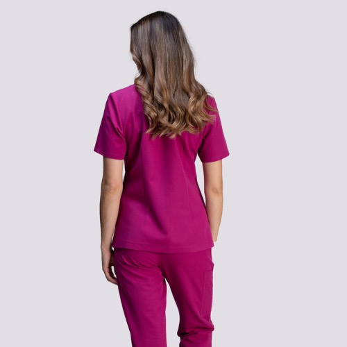 Tył kobiety w komplecie medycznym w kolorze fuksji; spodnie z kieszenią cargo i krótki rękaw bluzy. Włosy brązowe, lekko falowane, sięgają ramion.