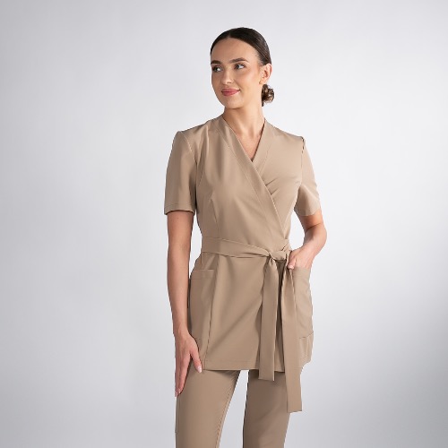 Kremowy komplet damski: tunika z wiązaniem w pasie i spodnie. Elegancki uniform w neutralnym odcieniu, idealny jako odzież dla personelu medycznego lub kosmetycznego.