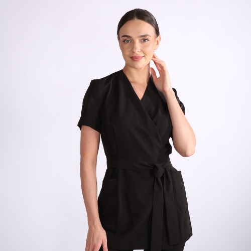 Kobieta prezentuje czarny, wiązany uniform medyczny z krótkim rękawem na białym tle. Elegancki i profesjonalny strój dla personelu medycznego.